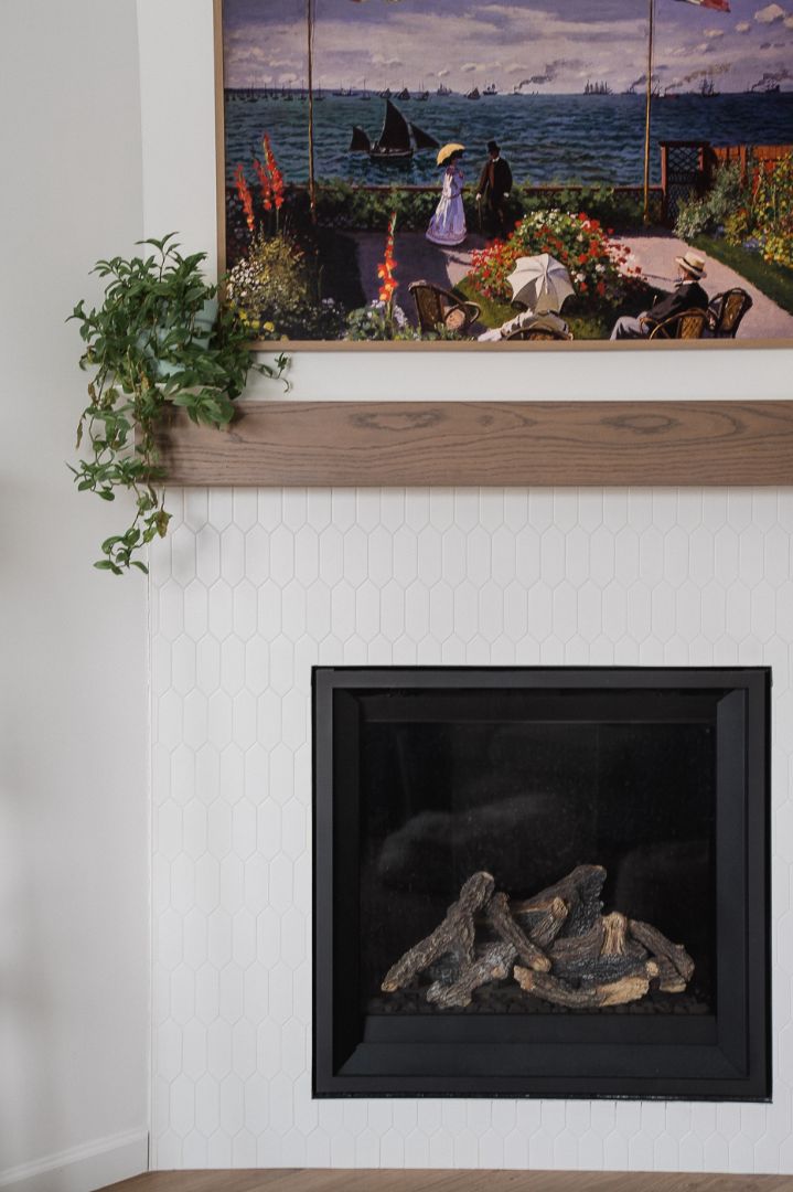 White tile fireplace with wood mantel and framed seascape artwork. in Calgary | Kavaleer Renovations White tile fireplace with wood mantel and framed seascape artwork. in Calgary | Kavaleer Renovations
